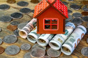 House on top of american dollars banknotes rolled into tube and many us coins. Home cash and saving.